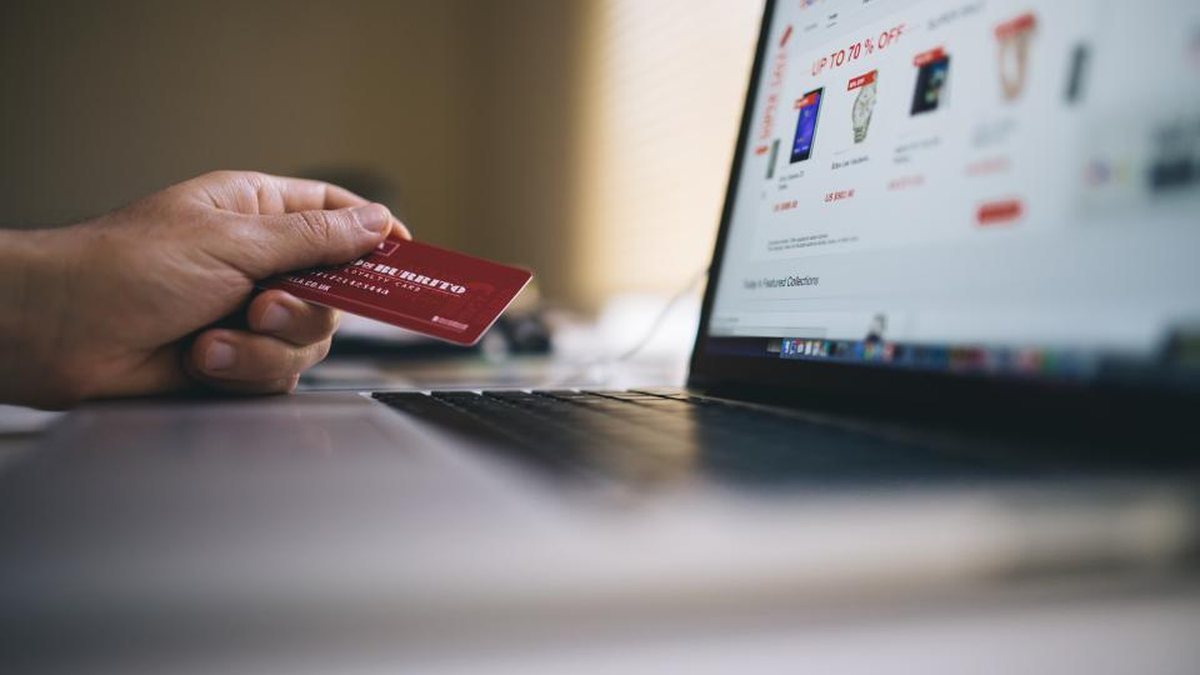 Hand holding a credit card at a laptop showing an online store