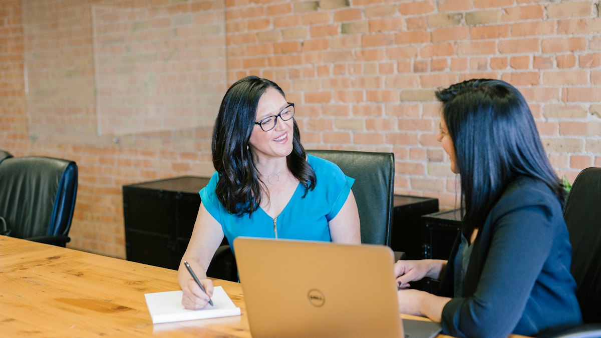 Two women talking across a table in a bright office