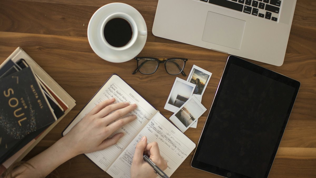Notebook, coffee and tablet on a desk while a person takes notes
